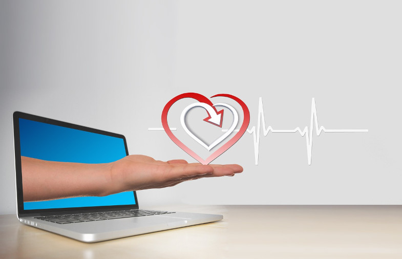 Eine Hand kommt aus dem Display eines Laptops. Stehend auf der Handfläche: Ein Herz und eine EKG-Sinuskurve.